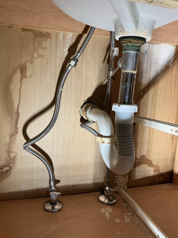 Completed installation of new bathroom sink faucet assembly with modern single-lever pull-out design in brushed nickel finish, including mounting plate and drain hardware. Replaced deteriorating P-trap assembly beneath sink due to visible corrosion and evidence of previous water leakage, installing new white plastic trap with proper sealing connections. Connected chrome braided supply line to ensure proper water flow to new faucet fixture.