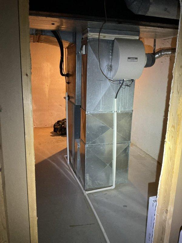 Responded to service call for burning smell when AC system is turned on at new residence. Upon inspection, identified Rheem gas furnace (Model KG50T100CELM1, Serial A161K12701) with central air conditioning system located in unfinished basement. System was operational and cooling properly despite odor complaint. Conducted thorough visual inspection of air handler, ductwork, and humidifier assembly. Documented equipment specifications and current condition with photos. Burning smell is consistent with dust accumulation on heat exchanger from furnace sitting idle during warmer months, which typically dissipates after initial AC usage. Verified all electrical connections secure, ductwork properly sealed, and no visible signs of overheating or component failure. Advised that odor should resolve naturally with continued operation, but to contact immediately if smell persists or worsens.