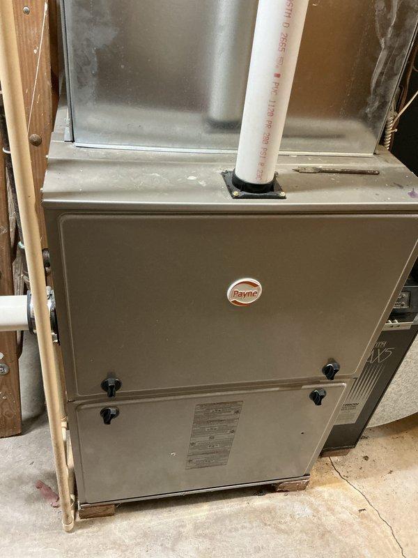 Completed comprehensive HVAC system replacement estimate for residential property requiring furnace, air conditioning unit, and steam humidifier installation. Existing Payne brand furnace located in basement showing operational wear with air handler/coil assembly requiring full replacement. Assessment identified need for new refrigerant lineset installation above ceiling to accommodate updated equipment specifications. Documented existing ductwork configuration including horizontal supply lines and vertical PVC venting system. Observed condensation and frost accumulation on existing refrigerant lines indicating active system operation during inspection. Evaluated mechanical room layout and clearances for proposed equipment installation, noting concrete floor mounting surface and proximity to unfinished wall framing. Photographed current system components including furnace cabinet, ductwork connections, and refrigerant piping for replacement specifications. Provided equipment sizing rec