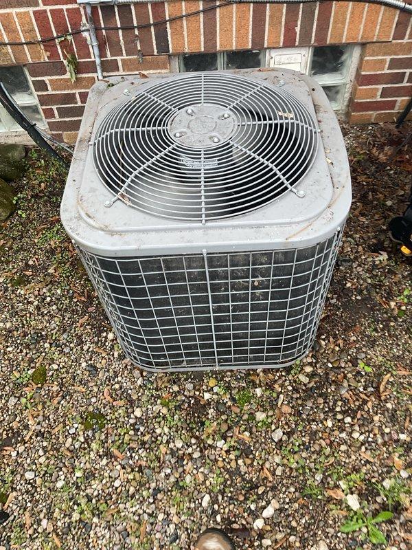 Completed comprehensive Gold Plan AC inspection on 10+ year old single-unit residential HVAC system with air handler located in basement. Inspected outdoor condenser unit showing age-appropriate wear and weathering on exterior cabinet, verified proper gravel pad placement and clearances around unit. Examined air filter installed in basement air handler, noting distinctive pleated media construction with proper fitment in housing frame. Verified system operational status with equipment running normally at time of inspection. Documented equipment condition through photographic records showing condenser unit exterior, fan grille assembly, and filter installation. All major components inspected and found functioning as designed with no immediate service requirements identified during routine maintenance visit.
