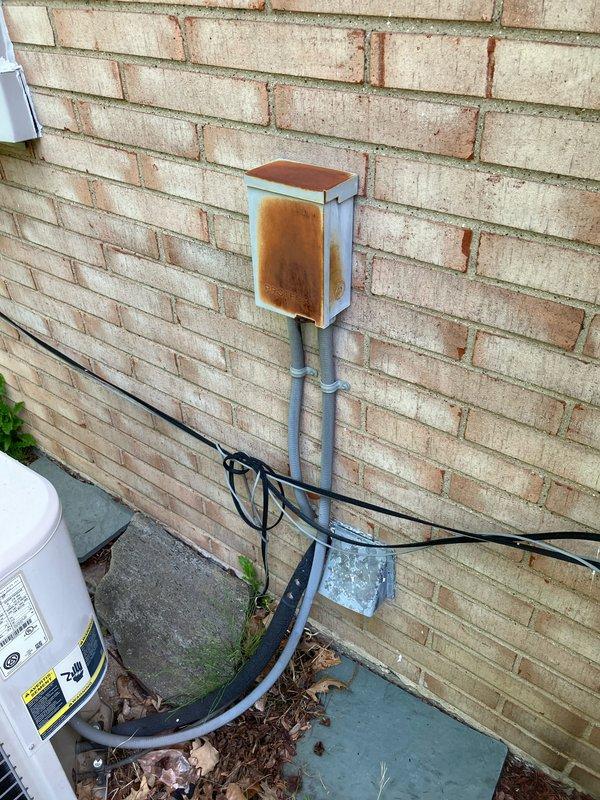 Conducted comprehensive assessment of existing R22 air conditioning system with compressor drawing excessive amperage, indicating imminent failure. Evaluated 10+ year old unit with air handler located in basement and outdoor condenser mounted on concrete pad against brick exterior. Provided complete system replacement estimate due to obsolete R22 refrigerant and failing compressor components. Documented existing electrical disconnect box showing significant corrosion and weathering requiring attention during replacement. Noted condenser area surrounded by debris, vegetation overgrowth, and organic matter requiring clearance prior to new equipment installation to ensure proper airflow and system efficiency. Advised that replacement installation scheduling dependent on favorable weather conditions above 65 degrees and dry conditions for optimal equipment setup and system commissioning.