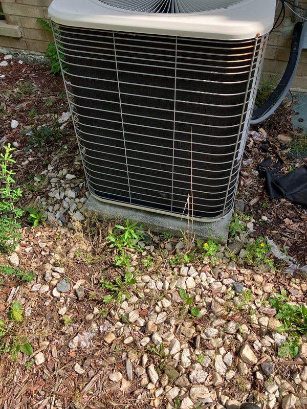 Conducted comprehensive assessment of existing R22 air conditioning system with compressor drawing excessive amperage, indicating imminent failure. Evaluated 10+ year old unit with air handler located in basement and outdoor condenser mounted on concrete pad against brick exterior. Provided complete system replacement estimate due to obsolete R22 refrigerant and failing compressor components. Documented existing electrical disconnect box showing significant corrosion and weathering requiring attention during replacement. Noted condenser area surrounded by debris, vegetation overgrowth, and organic matter requiring clearance prior to new equipment installation to ensure proper airflow and system efficiency. Advised that replacement installation scheduling dependent on favorable weather conditions above 65 degrees and dry conditions for optimal equipment setup and system commissioning.