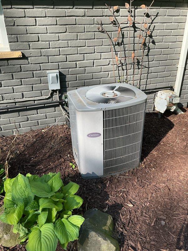 Performed comprehensive tune-up and inspection on Carrier brand air conditioning system with outdoor condensing unit located at exterior brick wall and air handler in attic space. Inspected refrigerant lines running along exterior wall, verified proper insulation and mounting, checked condenser coil fins for debris and damage, and tested fan operation. Accessed attic-mounted air handling equipment via attic access, inspected flexible ductwork for proper connection and airflow, verified adequate clearance around equipment, and checked insulation levels throughout attic space. All components operating within normal parameters at time of inspection.