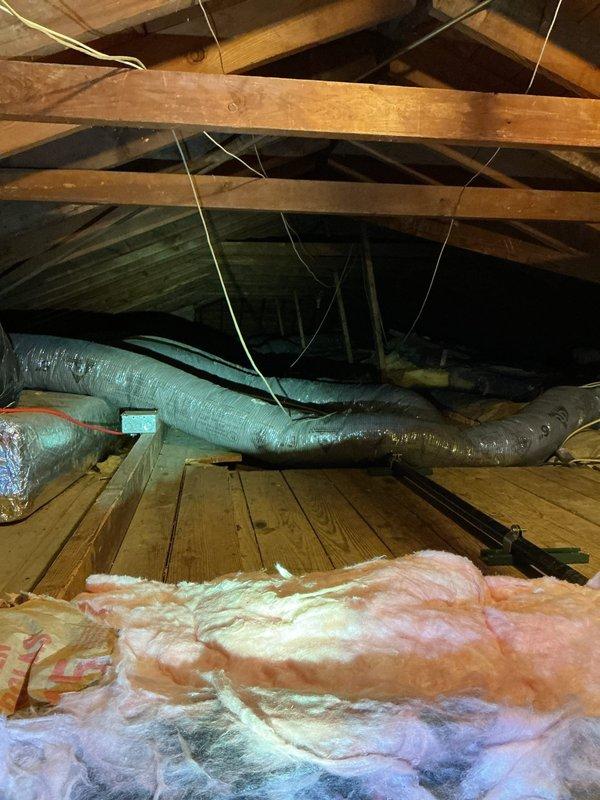 Performed comprehensive tune-up and inspection on Carrier brand air conditioning system with outdoor condensing unit located at exterior brick wall and air handler in attic space. Inspected refrigerant lines running along exterior wall, verified proper insulation and mounting, checked condenser coil fins for debris and damage, and tested fan operation. Accessed attic-mounted air handling equipment via attic access, inspected flexible ductwork for proper connection and airflow, verified adequate clearance around equipment, and checked insulation levels throughout attic space. All components operating within normal parameters at time of inspection.
