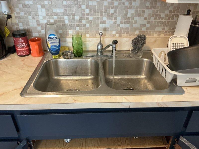 Responded to a water leak under the kitchen sink affecting the cold water supply line, which had been shut off for approximately six months. Upon inspection, identified a failed cold water supply line connection requiring replacement. Removed the defective flexible supply line, installed a new braided stainless steel supply hose, and reconnected it to the shut-off valve and faucet assembly. Restored cold water service to the kitchen sink, tested all connections for proper operation and leaks, and verified adequate water pressure and flow. Cabinet floor showed evidence of previous water damage from the extended leak period. Documented pre-repair and post-repair conditions with photographs.
