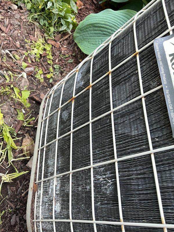 Responded to service call for inoperative air conditioning system. Upon arrival, inspected outdoor condensing unit located in landscaped area adjacent to residence. Unit appeared to be a residential split system with circular top grille design, showing signs of weathering and minor rust discoloration on protective metal components. Performed diagnostic assessment to determine cause of complete system failure and documented equipment condition with photographic evidence for service records.