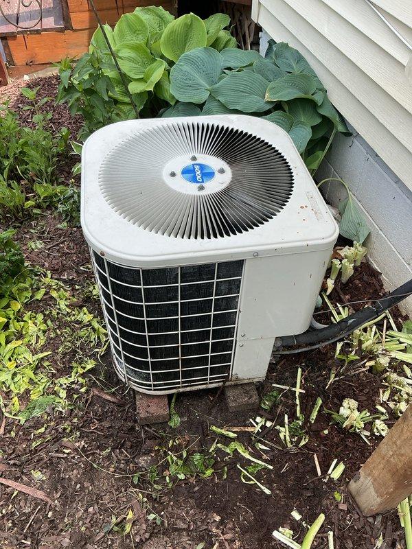 Responded to service call for inoperative air conditioning system. Upon arrival, inspected outdoor condensing unit located in landscaped area adjacent to residence. Unit appeared to be a residential split system with circular top grille design, showing signs of weathering and minor rust discoloration on protective metal components. Performed diagnostic assessment to determine cause of complete system failure and documented equipment condition with photographic evidence for service records.