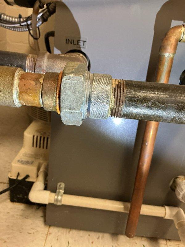 Responded to water leak complaint on 12-year-old hot water boiler located in basement. Upon inspection, identified failed gasket at brass pipe fitting connection causing active leak. Removed deteriorated gasket from hexagonal nut connector, replaced with new gasket, and reassembled plumbing connection. Tested system under pressure to confirm leak was resolved and all connections were secure.