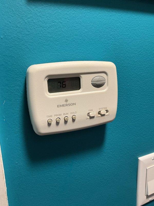 # HVAC Service Call - No Cooling Issue

Responded to service call for 3-year-old residential air conditioning system with no cooling. Upon arrival, verified thermostat was set to cooling mode and calling for 76°F. Inspected Emerson programmable thermostat mounted in living area and confirmed proper display function and settings.

Proceeded to outdoor condenser unit located on exterior concrete pad against brick wall. Performed visual inspection of unit exterior, noting clean condenser coil fins and secure top grille assembly. Verified electrical disconnect box and conduit connections at unit. Checked for proper power supply to condensing unit.

Conducted operational diagnostics on condensing unit including amperage draw, capacitor testing, and refrigerant pressure readings. Inspected evaporator coil assembly located in basement as indicated by customer. System found to have low refrigerant charge causing insufficient cooling capacity.

Located refrigerant leak at service port connectio