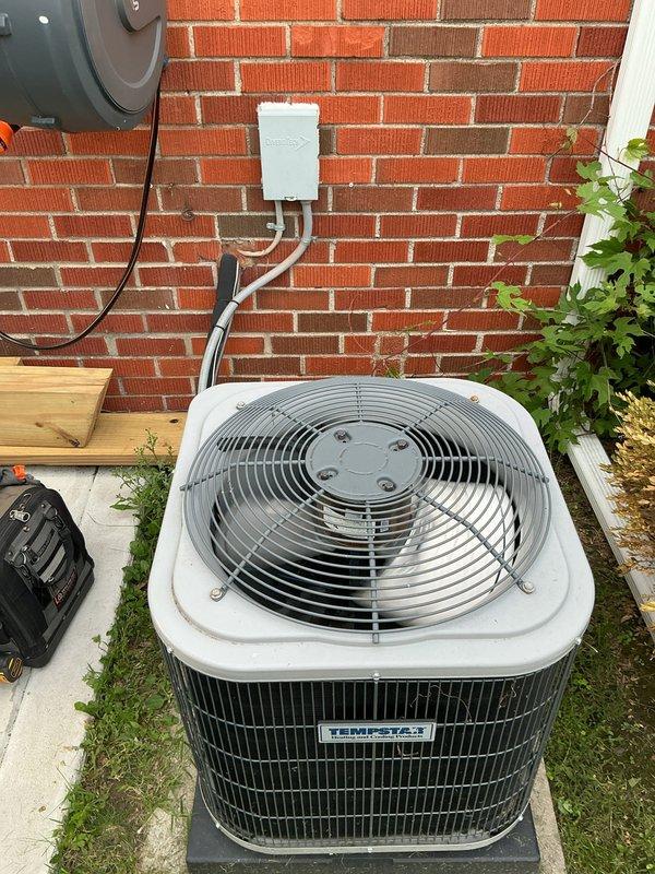 # HVAC Service Call - No Cooling Issue

Responded to service call for 3-year-old residential air conditioning system with no cooling. Upon arrival, verified thermostat was set to cooling mode and calling for 76°F. Inspected Emerson programmable thermostat mounted in living area and confirmed proper display function and settings.

Proceeded to outdoor condenser unit located on exterior concrete pad against brick wall. Performed visual inspection of unit exterior, noting clean condenser coil fins and secure top grille assembly. Verified electrical disconnect box and conduit connections at unit. Checked for proper power supply to condensing unit.

Conducted operational diagnostics on condensing unit including amperage draw, capacitor testing, and refrigerant pressure readings. Inspected evaporator coil assembly located in basement as indicated by customer. System found to have low refrigerant charge causing insufficient cooling capacity.

Located refrigerant leak at service port connectio