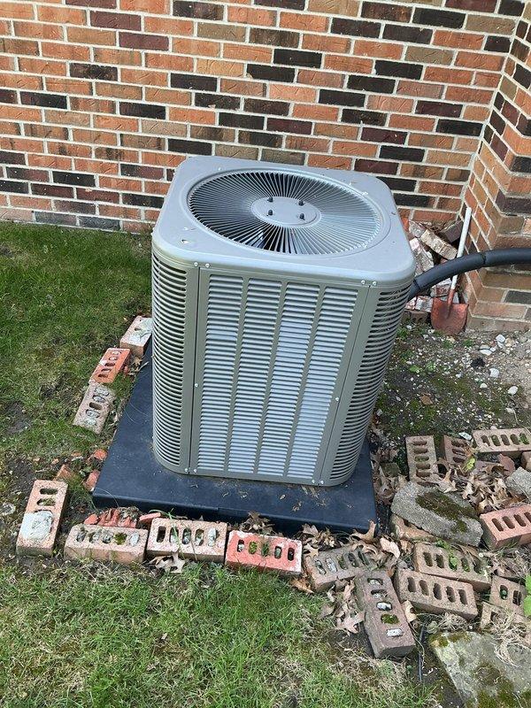 Completed Gold AC Inspection on residential air conditioning system less than 10 years old. Unit is positioned on concrete pad against exterior brick wall with refrigerant lines properly insulated and routed. Performed comprehensive system evaluation including visual inspection of condenser unit exterior condition, fan grille, and louvered panels. Documented equipment installation and surrounding area conditions with photographic records for service history. System operational parameters verified and equipment found to be functioning within manufacturer specifications.