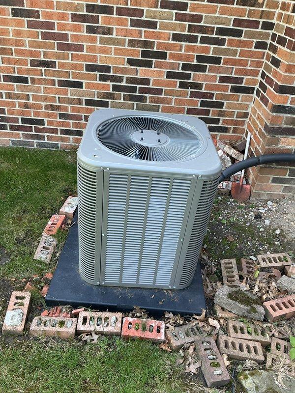 Completed Gold AC Inspection on residential air conditioning system less than 10 years old. Unit is positioned on concrete pad against exterior brick wall with refrigerant lines properly insulated and routed. Performed comprehensive system evaluation including visual inspection of condenser unit exterior condition, fan grille, and louvered panels. Documented equipment installation and surrounding area conditions with photographic records for service history. System operational parameters verified and equipment found to be functioning within manufacturer specifications.