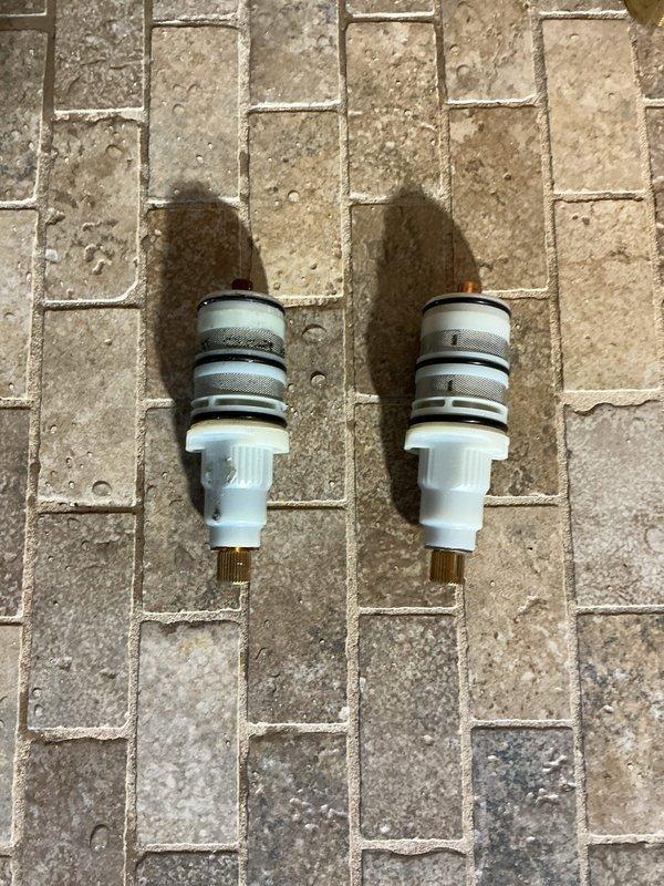 Replaced worn shower valve cartridges showing mineral buildup and deposits on the fixture assembly. Removed existing cartridges from the shower control valve, installed two new replacement cartridge units with mesh filtration components, and reassembled the octagonal escutcheon plate fixture to restore proper water flow and temperature control functionality.