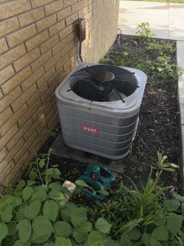 Completed comprehensive Gold AC Inspection on 10+ year old Bryant outdoor condensing unit at residential property. Performed visual inspection of exterior condenser unit positioned on concrete pad against building foundation, confirming proper clearance and adequate airflow around equipment. Utilized digital clamp meter to measure electrical parameters including voltage and amperage draw at condensing unit, verifying proper electrical function and system performance. Inspected condenser coil fins for debris accumulation, damage, or blockage that could restrict airflow. Verified operation of condenser fan motor and compressor. Checked refrigerant line connections and electrical disconnect box mounted on exterior wall. Confirmed unit operational with no visible damage, excessive wear, or safety concerns noted. Equipment operating within normal parameters at time of inspection with air handler/coil located in basement area.