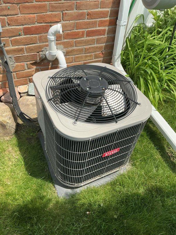 Completed comprehensive Gold AC Inspection on a 2013 residential air conditioning system with outdoor condenser unit and basement-located air handler. Performed thorough multi-point inspection of condenser unit positioned on concrete pad against exterior brick wall, verifying proper operation of top-mounted fan, examining condenser coil fins for debris and damage, checking refrigerant line connections, and inspecting PVC condensate drain routing. System found to be in operational condition with no immediate service concerns identified. Unit exterior components, including protective fan grille and coil fins, showed normal wear for age with no visible corrosion or structural damage. Condensate drainage system properly routed and functioning as designed.