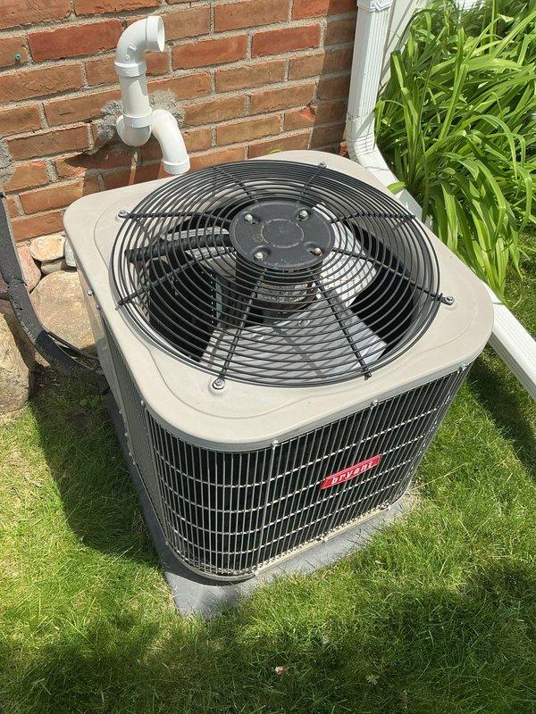 Completed comprehensive Gold AC Inspection on a 2013 residential air conditioning system with outdoor condenser unit and basement-located air handler. Performed thorough multi-point inspection of condenser unit positioned on concrete pad against exterior brick wall, verifying proper operation of top-mounted fan, examining condenser coil fins for debris and damage, checking refrigerant line connections, and inspecting PVC condensate drain routing. System found to be in operational condition with no immediate service concerns identified. Unit exterior components, including protective fan grille and coil fins, showed normal wear for age with no visible corrosion or structural damage. Condensate drainage system properly routed and functioning as designed.