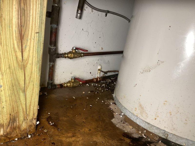 Responded to water leak in utility area with standing water on floor. Upon inspection, identified source of leak from plumbing connections near water heater. Shut off water supply using existing brass shut-off valves and assessed extent of water damage to surrounding area. Tightened loose connections on copper piping and replaced deteriorated hose clamp on water heater inlet line. Tested all connections under pressure to verify leak was resolved. Recommended follow-up maintenance to address accumulated debris and grime on mechanical components to prevent future issues.