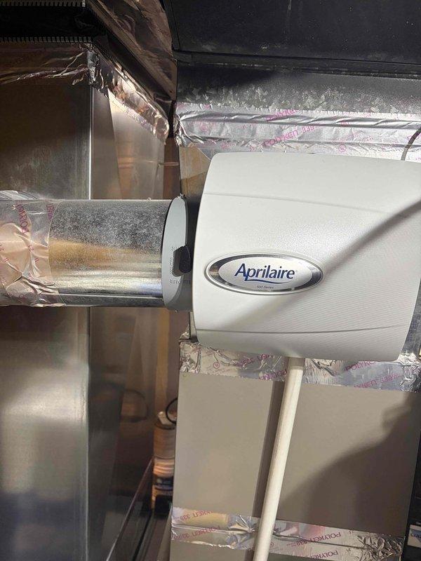 Completed comprehensive Gold AC inspection on 4-year-old residential air conditioning system with air handler located in basement. Verified system operational status and confirmed single-unit configuration with homeowner present. Performed thorough examination of all major components including air handler, ductwork, Aprilaire humidifier integration, condensate pump assembly, and refrigerant line connections. Inspected metal ductwork for proper sealing and noted foil tape applications at joints. Evaluated condensate management system including white condensate pump with proper drainage configuration and PVC piping installation. Assessed humidifier mounting and connection to main duct system. Documented system condition through photographic records showing equipment installation, ductwork integrity, and mechanical room layout. All components found in working order with system performing within normal parameters.