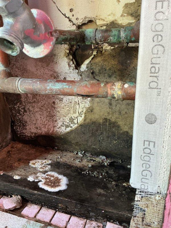 Completed warranty service for freeze-damaged plumbing components. Inspected and documented severely corroded copper piping and fittings showing extensive verdigris corrosion and deterioration from freeze break conditions. Assessed water-damaged wall surfaces with significant structural deterioration, mineral deposits, and moisture intrusion around affected plumbing installation.