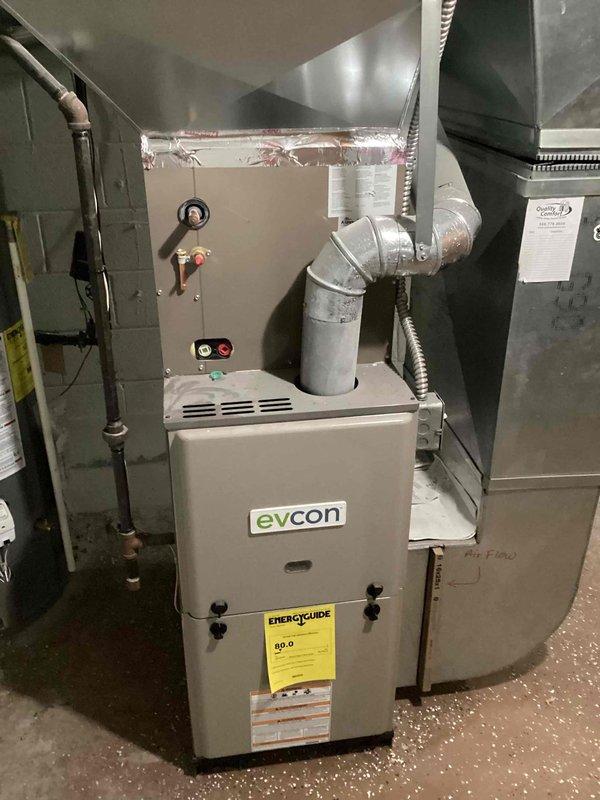 Provided estimate for complete HVAC system replacement at residential property where existing 10+ year old air conditioning unit is non-operational. Evaluated basement-installed Evcon natural gas furnace and associated ductwork, photographed current equipment configuration including exterior foundation area where new condensing unit would be located. Documented existing system components, ductwork connections, and proposed installation site marked in foundation garden bed area to prepare comprehensive replacement quote for new air conditioning system compatible with existing natural gas heating equipment.