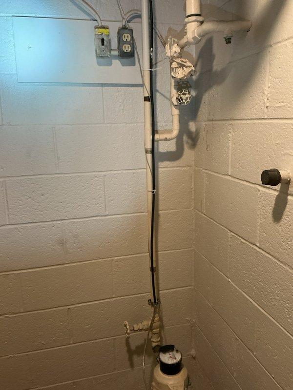 Responded to service call for slow water leak occurring at interior irrigation valve in 70-year-old home. Upon inspection, identified leak originating from aged brass valve assembly connected to outdoor irrigation system, with water dripping at rate of approximately one drop every few seconds when valve was in open position. Leak was isolated to valve stem packing and associated pipe fittings showing significant corrosion and oxidation consistent with age of plumbing system. Inspected water meter assembly and associated copper supply lines mounted on basement wall, noting advanced deterioration of valve components and compromised pipe connections. Documented existing plumbing configuration including corroded brass fittings, aged copper piping, and meter installation. Assessed condition of irrigation shutoff valve and surrounding pipe joints for extent of water damage and potential failure points. Provided customer with photographic documentation of leak source and recommendations for v