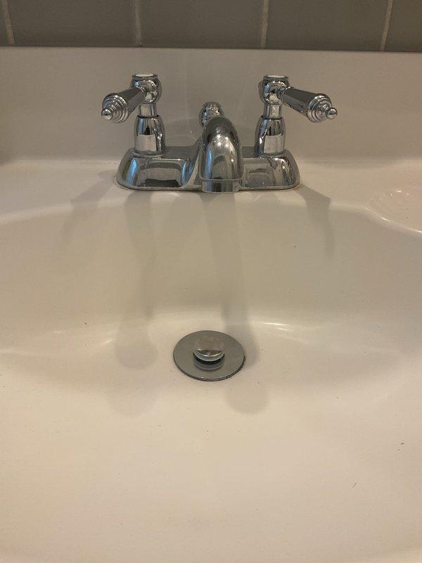 Completed installation of chrome two-handle bathroom faucet with porcelain lever handles on existing white porcelain sink. Verified proper water flow, tested both hot and cold supply lines, and ensured pop-up drain assembly operates correctly with no leaks detected.