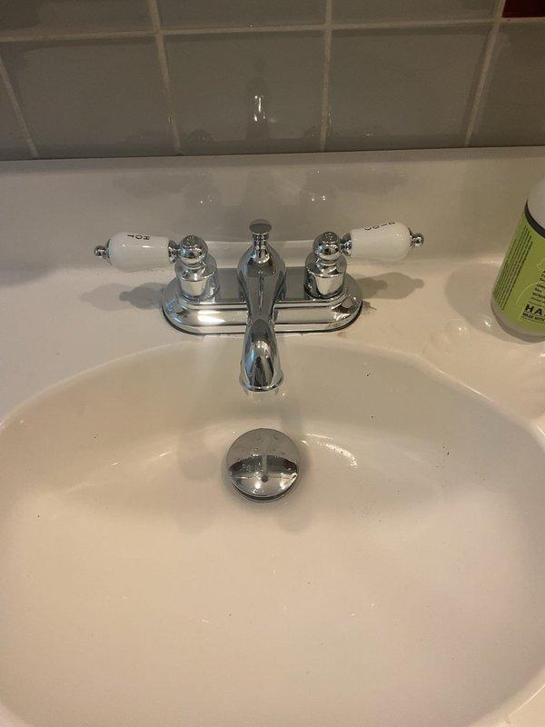 Completed installation of chrome two-handle bathroom faucet with porcelain lever handles on existing white porcelain sink. Verified proper water flow, tested both hot and cold supply lines, and ensured pop-up drain assembly operates correctly with no leaks detected.