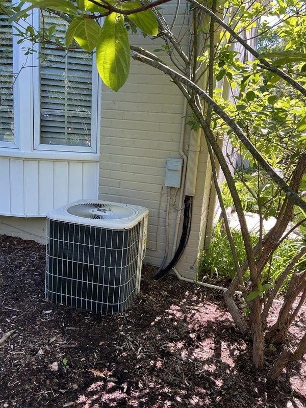 Completed Gold AC inspection on residential property with two HVAC systems: a 25-year-old attic unit utilizing R22 refrigerant and a 12-year-old unit with air handler/coil located in basement. Accessed attic unit using 6-foot ladder to perform comprehensive system evaluation. Documented exterior condensing unit condition through photographic inspection, noting cylindrical condenser configuration with white top cap and metal grille construction, mounted on mulch bed against residential siding with electrical disconnect box and conduit properly installed. Both systems confirmed operational at time of inspection, meeting prerequisites for estimate development on equipment replacement options.