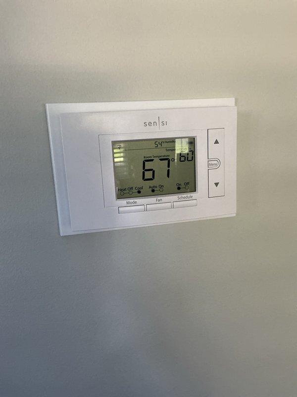 Completed comprehensive HVAC tune-up inspection on 2-year-old basement system, including thorough evaluation of heating equipment, humidifier operation, and thermostat functionality. Verified Sensi digital thermostat displaying proper temperature readings at 67°F with heat/cool mode controls operating correctly. Inspected water heater connections, exhaust venting, and safety valves with green handle valve confirmed in proper position; noted HVAC filter available on-site for replacement.