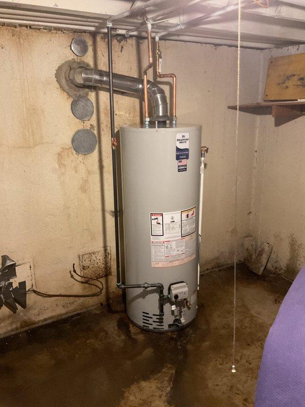 Completed installation of a 50-gallon standard tanked water heater in basement utility area. Unit was positioned against concrete block wall, with all supply lines, gas connections, and flue piping properly reconnected and secured to manufacturer specifications. Installation verified operational with all safety labels intact and visible.