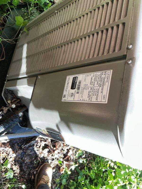 Completed comprehensive Gold AC inspection on 3-year-old single-unit air conditioning system with air handler located in basement. Verified system operational status, inspected outdoor condenser unit positioned on concrete pad with proper clearance, examined electrical disconnect box mounted on exterior brick wall, and confirmed all components functioning within normal parameters. Documented equipment condition through photographic records showing condenser unit, disconnect switch, and surrounding area with minor vegetation growth present but not obstructing airflow or access.
