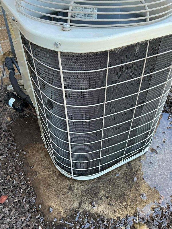 Completed Gold AC inspection on 22-year-old residential air conditioning system with air handler located in basement. Performed comprehensive evaluation of outdoor condenser unit, which is positioned on concrete pad against brick exterior wall with proper electrical disconnect box mounted above. Verified unit operational status, inspected heat exchanger coils, fan assembly, and protective grilles for proper condition and functionality. Documented equipment condition through photographic records showing condenser placement, surrounding landscape materials including decorative rock and soil, and overall system accessibility. Unit appears functional with normal aging characteristics for equipment of this vintage, with condenser properly secured on weathered concrete pad and adequate clearance maintained around perimeter for airflow.