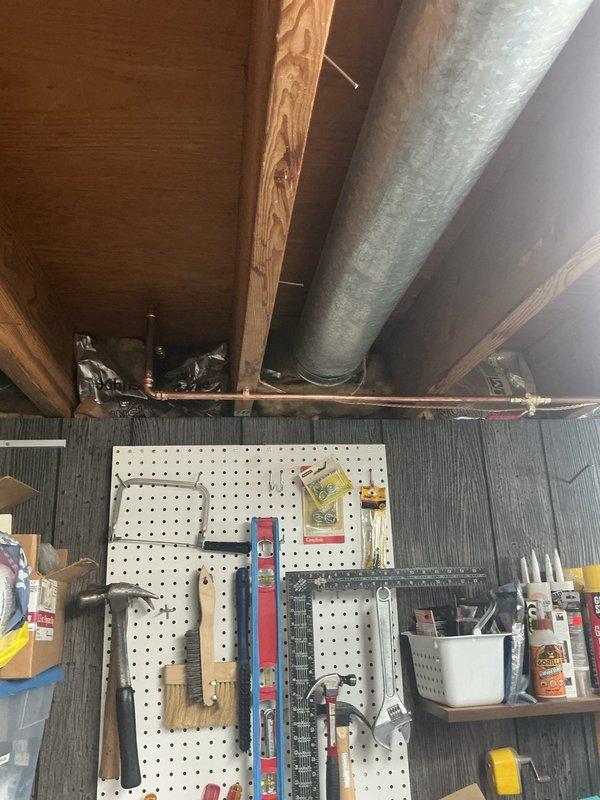 Accessed workshop plumbing system through existing wall opening to inspect and photograph concealed piping infrastructure. Located and documented galvanized ductwork, copper supply lines with shut-off valves (hot and cold), and PVC drainage piping within wall cavity. Verified proper installation and accessibility of plumbing components behind finished drywall surface for maintenance and future service requirements.