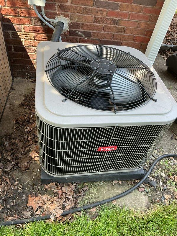 Completed comprehensive Gold AC inspection on 5-year-old air conditioning system with air handler located in basement. Inspected outdoor condensing unit positioned on concrete pad against exterior brick wall, noting unit operational with proper electrical connections and refrigerant lines secured. Advised customer that debris including fallen leaves and twigs surrounding condenser unit should be cleared to maintain optimal airflow and system efficiency.