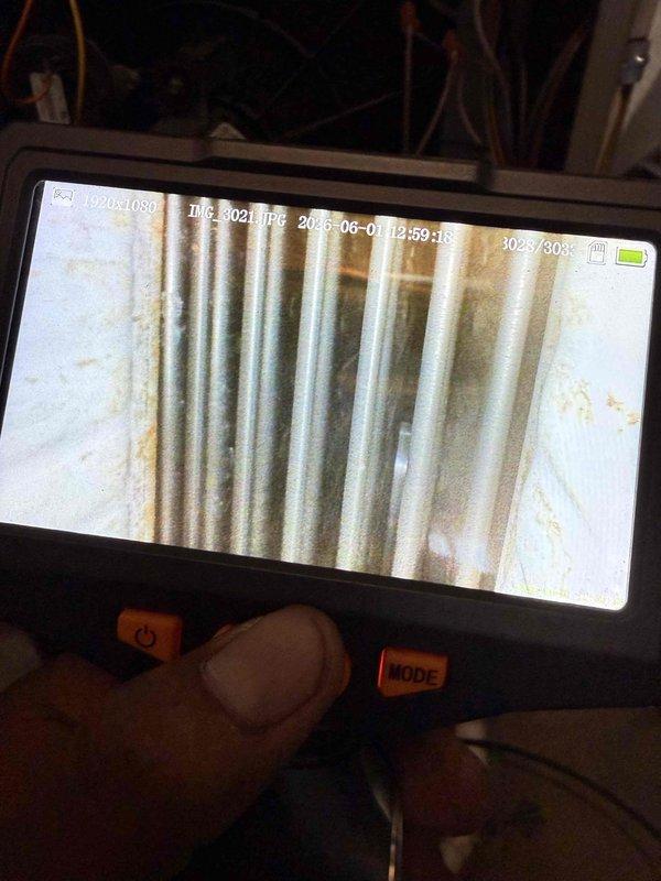 Responded to service call for 20-year-old A/C unit in basement experiencing unusual noises and overheating issues. Performed diagnostic testing using digital clamp meter on condenser unit, recording electrical readings of 280.0 amps and 0.52 voltage parameters. Conducted borescope inspection of internal components, revealing significant rust and corrosion on heat exchanger tubing and ductwork, consistent with age-related deterioration affecting system performance and causing reported operational concerns.