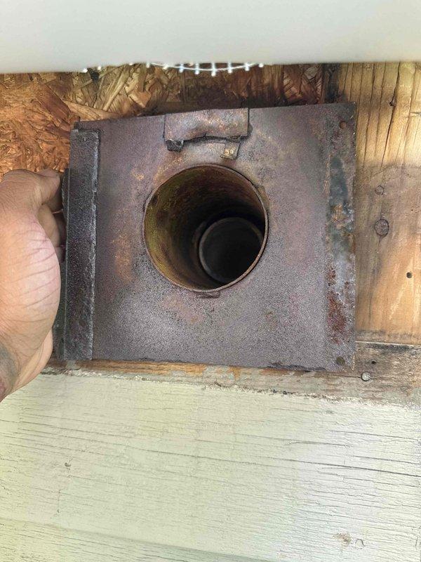 Responded to service call for charring wood observed around heating system vent pipe on building exterior. Upon arrival, inspected vent termination and discovered severely deteriorated metal flange plate with heavy rust and corrosion around circular vent opening. Wood framing surrounding the penetration showed significant charring and heat damage, indicating prolonged exposure to excessive heat or improper clearances. Documented conditions with photographs showing compromised flange integrity and damaged wood substrate. Verified heating system in basement remained operational at time of inspection. Assessed vent pipe installation and clearances to combustible materials. Recommended immediate replacement of deteriorated vent termination assembly and repair of charred wood framing to prevent potential fire hazard and ensure code compliance.
