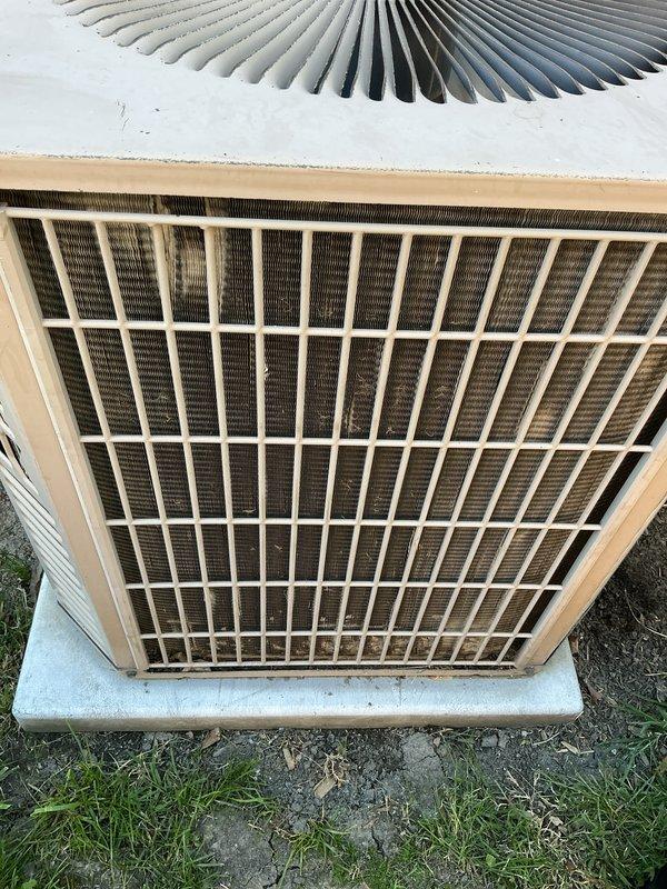 Completed Gold AC inspection on single outdoor condensing unit located on concrete pad in residential backyard. Performed comprehensive system evaluation including visual inspection of exterior housing, protective grille, and internal components. Noted moderate dirt and dust accumulation on condenser coils with brownish discoloration on cooling fins, consistent with normal aging and outdoor exposure. Inspected fan assembly and verified operational status. Unit showed signs of weathering including surface discoloration and minor exterior wear on beige-colored frame sections. Documented equipment condition with photographs showing hexagonal white/beige housing with protective metal grille, circular fan assembly with radial spoke pattern, and installation on weathered concrete pad adjacent to chain-link fence and brick wall. Confirmed equipment is currently operational and homeowner reported no performance issues. Air handler/coil located in basement. System appears to be functioning as d