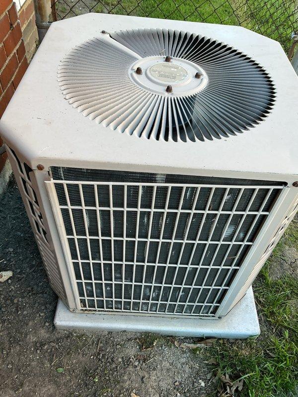 Completed Gold AC inspection on single outdoor condensing unit located on concrete pad in residential backyard. Performed comprehensive system evaluation including visual inspection of exterior housing, protective grille, and internal components. Noted moderate dirt and dust accumulation on condenser coils with brownish discoloration on cooling fins, consistent with normal aging and outdoor exposure. Inspected fan assembly and verified operational status. Unit showed signs of weathering including surface discoloration and minor exterior wear on beige-colored frame sections. Documented equipment condition with photographs showing hexagonal white/beige housing with protective metal grille, circular fan assembly with radial spoke pattern, and installation on weathered concrete pad adjacent to chain-link fence and brick wall. Confirmed equipment is currently operational and homeowner reported no performance issues. Air handler/coil located in basement. System appears to be functioning as d