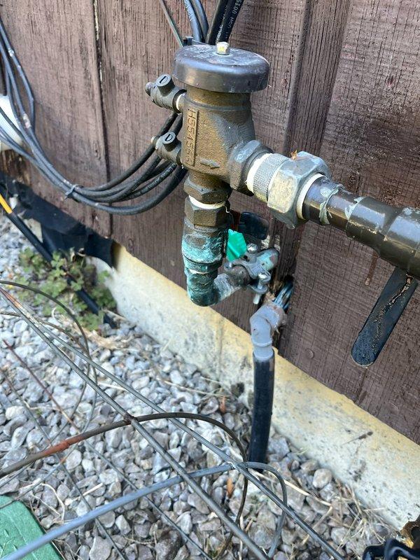 Completed annual backflow prevention device testing on exterior water supply system per regulatory requirements. Inspected and tested brass backflow preventer assembly mounted against perimeter fence, verifying proper operation of check valves, test cocks, and shut-off valves. Device showed age-appropriate weathering and patina but maintained functional integrity and passed certification testing. Documented equipment condition with photographs for compliance records.