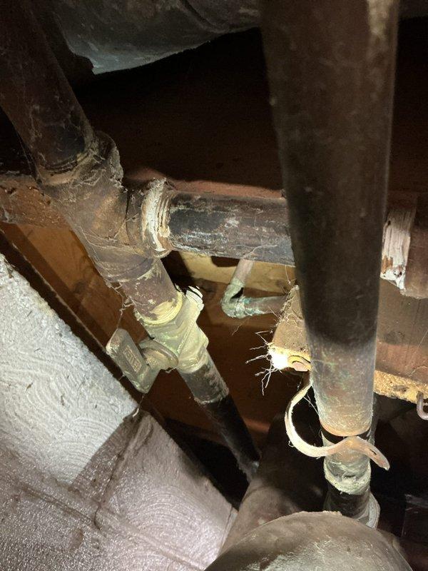 Responded to service call for gas line repairs connecting to hot water heater in basement utility area. Upon inspection, identified aging yellow flexible gas line running along concrete floor to water heater with connections requiring attention. Assessed existing plumbing infrastructure including corroded copper piping with significant oxidation, green-blue patina, and mineral deposits around joints and fittings. Performed necessary repairs to gas line connection at hot water heater to ensure safe and proper operation. Verified all connections were secure and tested system for leaks. Work completed in basement mechanical room containing water heater, HVAC unit, and washing machine with exposed ceiling joists and concrete block walls.