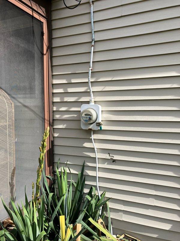 Performed diagnostic evaluation on a four-year-old residential air conditioning system with suspected compressor failure and defective outdoor fan motor. Unit remained operational during inspection but was determined to be out of manufacturer warranty. Documented existing equipment condition with photographs of the outdoor condensing unit installed on rock bed adjacent to home foundation, including electrical meter location and refrigerant line routing. Provided comprehensive replacement estimate for complete system due to failed components and warranty status.