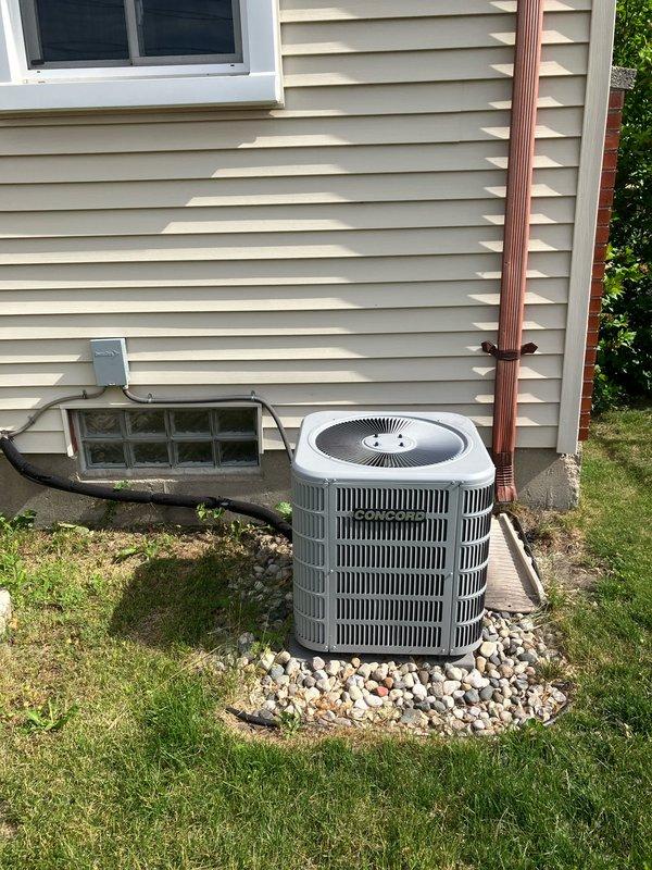 Performed diagnostic evaluation on a four-year-old residential air conditioning system with suspected compressor failure and defective outdoor fan motor. Unit remained operational during inspection but was determined to be out of manufacturer warranty. Documented existing equipment condition with photographs of the outdoor condensing unit installed on rock bed adjacent to home foundation, including electrical meter location and refrigerant line routing. Provided comprehensive replacement estimate for complete system due to failed components and warranty status.