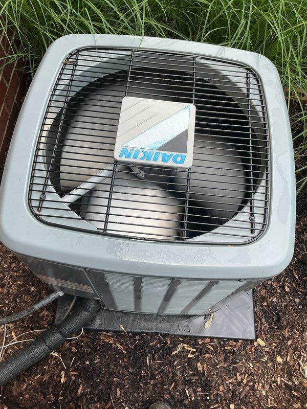Completed comprehensive AC inspection on multi-unit residential system with 4-year-old Daikin equipment. Inspected outdoor condenser units positioned in landscaped area with mulch bedding, verified proper fan operation, checked refrigerant lines and electrical connections, and documented equipment condition with protective grilles intact and functioning normally. Air handler/coil located in basement was assessed, and all components found to be operating within normal parameters with no immediate service needs identified.