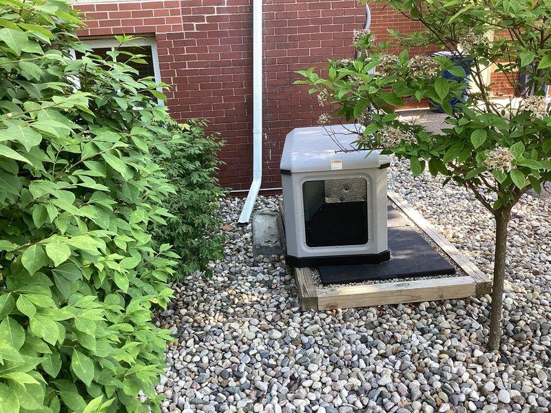 Responded to service call for 22 KW Briggs and Stratton generator reported to be sliding off its base. Upon arrival, inspected generator mounting system and found unit positioned on wooden platform with black rubber isolation pad over river rock bed against building exterior. Evaluated platform stability, verified proper positioning of isolation pad, and assessed structural integrity of wooden base frame. Confirmed generator secure on mounting surface with proper clearances maintained for ventilation and service access. Unit operational and stable on platform following inspection.
