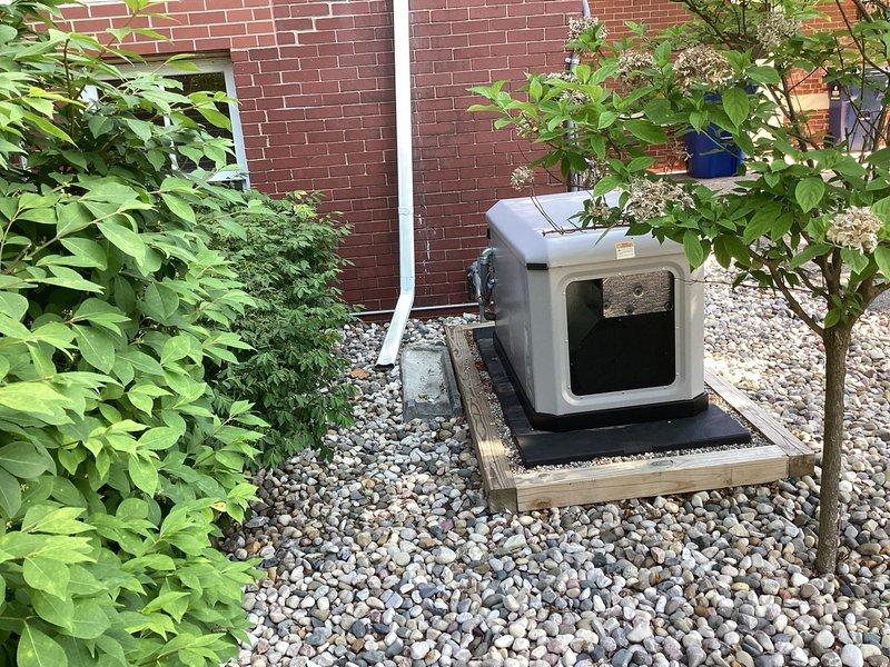 Responded to service call for 22 KW Briggs and Stratton generator reported to be sliding off its base. Upon arrival, inspected generator mounting system and found unit positioned on wooden platform with black rubber isolation pad over river rock bed against building exterior. Evaluated platform stability, verified proper positioning of isolation pad, and assessed structural integrity of wooden base frame. Confirmed generator secure on mounting surface with proper clearances maintained for ventilation and service access. Unit operational and stable on platform following inspection.