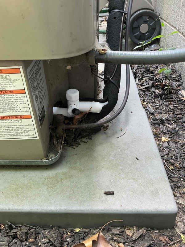 Responded to service call for central air conditioning system experiencing inadequate cooling and ice formation on refrigerant lines. Upon arrival, conducted visual inspection of outdoor condenser unit and associated components. Observed ice buildup on suction line, indicating potential refrigerant flow restriction or low charge condition. Checked system operation and verified unit was running but not achieving proper cooling capacity. Inspected condenser coil, fan operation, and electrical connections. Evaluated refrigerant line insulation and condensate drainage system. Documented equipment condition through photographs showing outdoor heat pump unit on concrete pad with PVC condensate piping, insulated refrigerant lines, and top-mounted fan assembly. Unit appeared in generally well-maintained condition with no visible signs of significant physical damage or corrosion. Identified ice formation issue as likely caused by restricted airflow, low refrigerant charge, or metering device ma