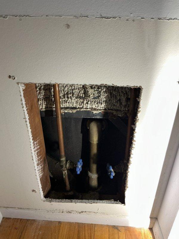 Responded to a dripping shower faucet in a second-floor bathroom of a 1970s-era home. Created access panel in wall to expose plumbing infrastructure and shut-off valves. Replaced worn shower valve assembly and cartridge that had been leaking for approximately two weeks. Addressed minor drip at bathroom sink faucet by replacing worn washers and seals. Installed new blue-handled shut-off valves on supply lines for improved future access and maintenance. Tested all fixtures for proper operation and verified no leaks present. Access panel left open for inspection, ready for drywall repair and finishing upon approval.