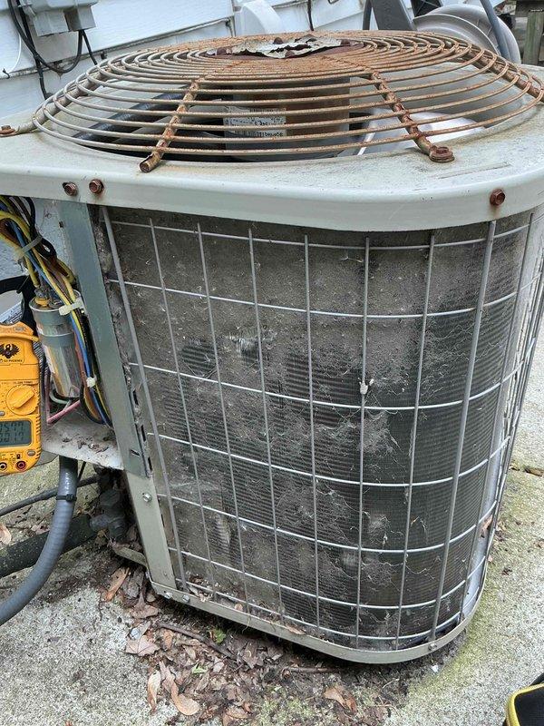 Responded to no cooling call on outdoor condensing unit. Upon arrival, found unit with significant weathering and corrosion, including heavily rusted fan guard and deteriorated exterior components. Performed diagnostic testing with multimeter to assess electrical functionality and compressor operation. Documented extensive rust damage on fan guard assembly, mounting hardware, and housing, along with heavily soiled condenser coil filter requiring cleaning or replacement for proper airflow and system efficiency.