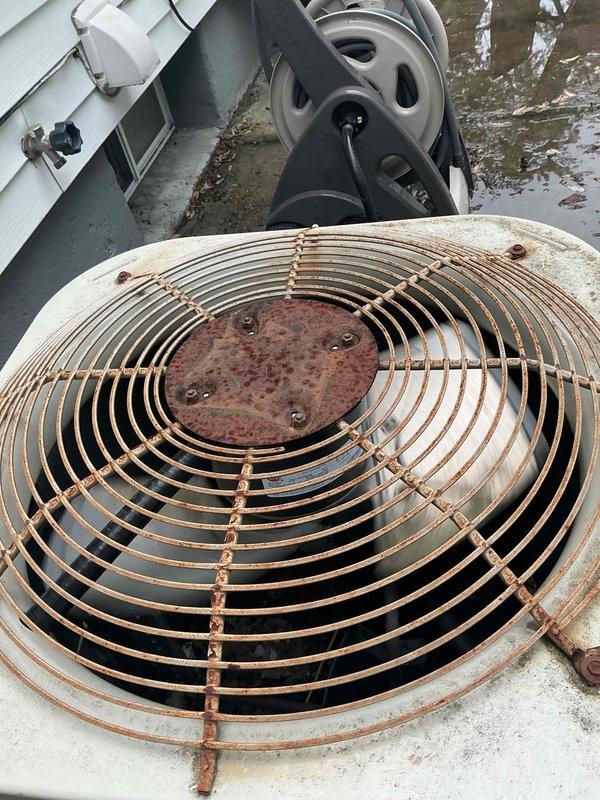 Responded to no cooling call on outdoor condensing unit. Upon arrival, found unit with significant weathering and corrosion, including heavily rusted fan guard and deteriorated exterior components. Performed diagnostic testing with multimeter to assess electrical functionality and compressor operation. Documented extensive rust damage on fan guard assembly, mounting hardware, and housing, along with heavily soiled condenser coil filter requiring cleaning or replacement for proper airflow and system efficiency.