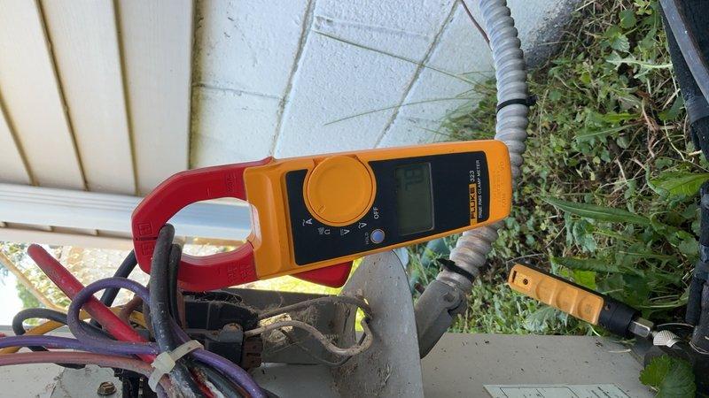Responded to service call for central air conditioning unit repeatedly blowing fuses after 1-2 hours of operation. Upon arrival, accessed 10+ year old outdoor condensing unit located in backyard. Performed comprehensive electrical diagnostics using clamp meter and multimeter to measure amperage draw, voltage, and resistance across compressor, condenser fan motor, and capacitor circuits. Testing revealed abnormal electrical readings indicating potential compressor short cycling or capacitor failure causing excessive current draw and subsequent fuse failure. Documented electrical measurements and equipment condition with photos showing active diagnostic testing in progress. Unit operational at time of inspection but requires further component testing or replacement to resolve intermittent overcurrent condition causing repeated fuse failures.